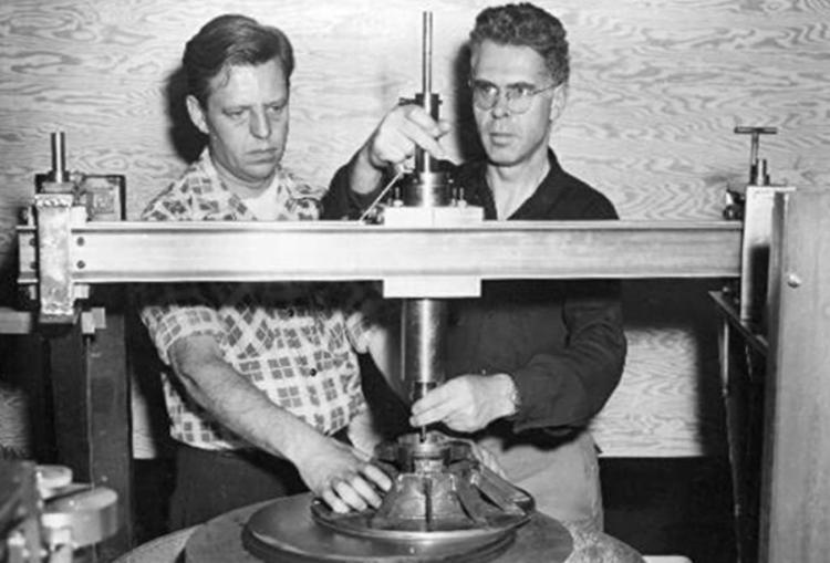 1951: The delicate job of grinding a 16 inch lens for an 'inside-out' telescope or coronagraph is under way in the Boulder optical shop of HAO. Pictured adjusting the grinding mechanism are Frederick B. Pearson (left) chief optician for the observatory, and Dr. John W. Evans, noted optical physicist and member of the observatory staff. Two 26 foot coronagraphs, the world's largest, were then under construction by the Westinghouse Electric Corporation at Sunnyvale, California. The instruments were used for solar research programs conducted by HAO, which at that time was affiliated with Harvard University, Harvard College Observatory, and the University of Colorado.